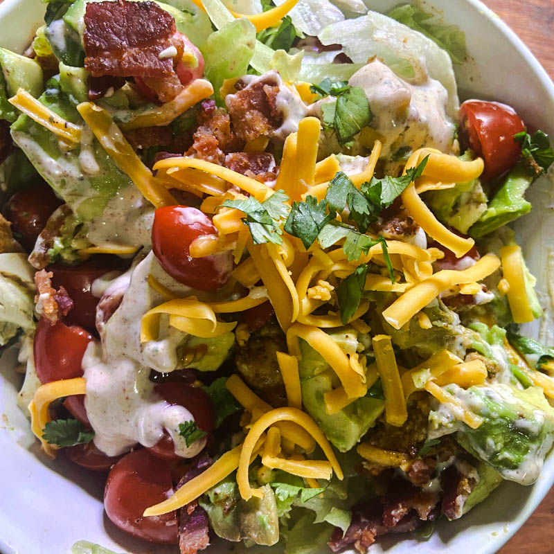 Cajun Chicken Cobb Salad with iceberg lettuce, avocado, bacon, cherry tomatoes, and cheddar cheese, topped with Cajun Ranch dressing.