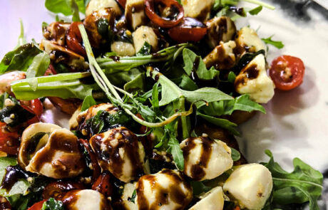 Caprese bruschetta with mozzarella, tomatoes, arugula, and balsamic glaze on a toasted bread slice.