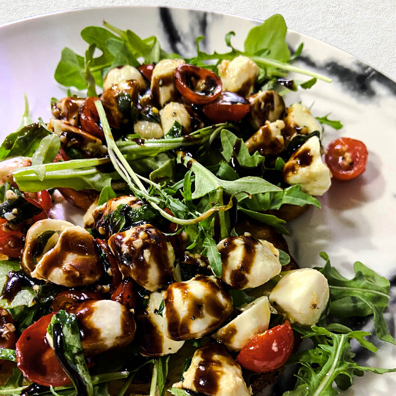 Caprese bruschetta with mozzarella, tomatoes, arugula, and balsamic glaze on a toasted bread slice.