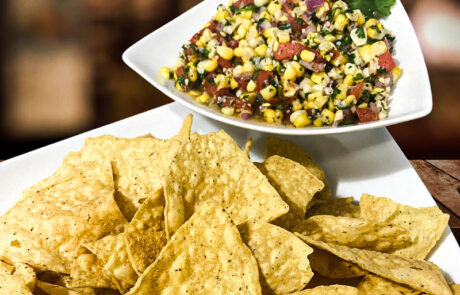 Corn salsa served with tortilla chips, featuring tomatoes, onions, cilantro, and corn.