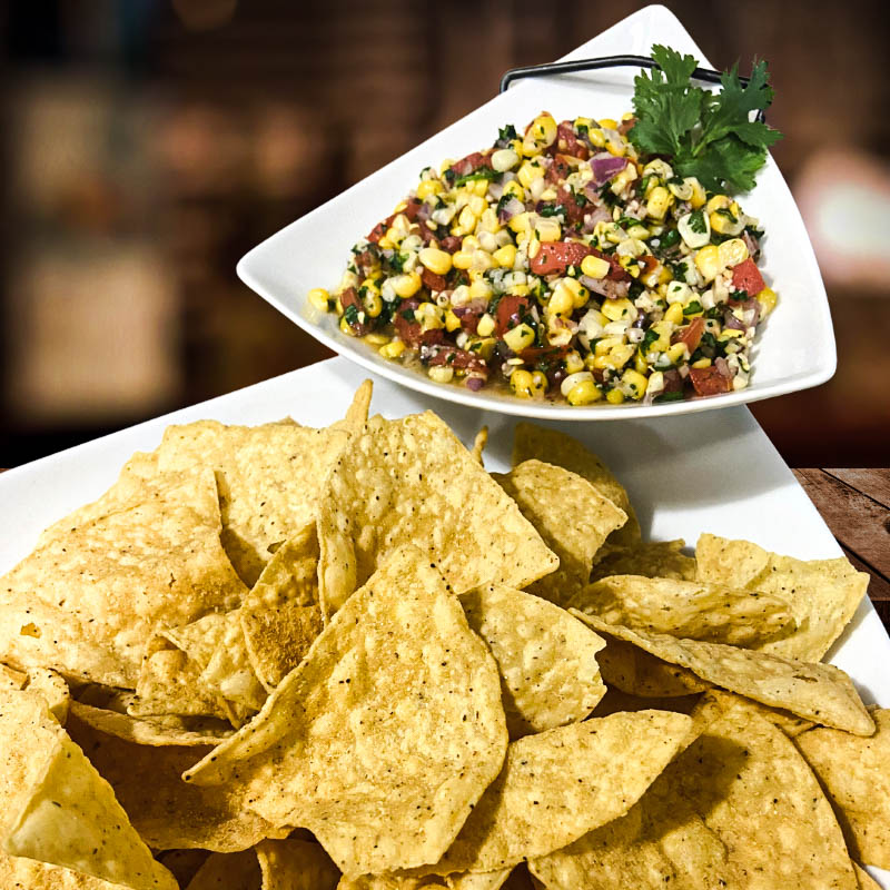 Corn salsa served with tortilla chips, featuring tomatoes, onions, cilantro, and corn.