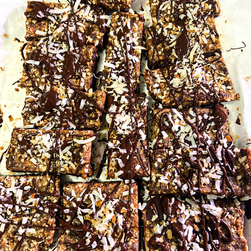 Date and coconut bars topped with melted dark chocolate and toasted coconut flakes.